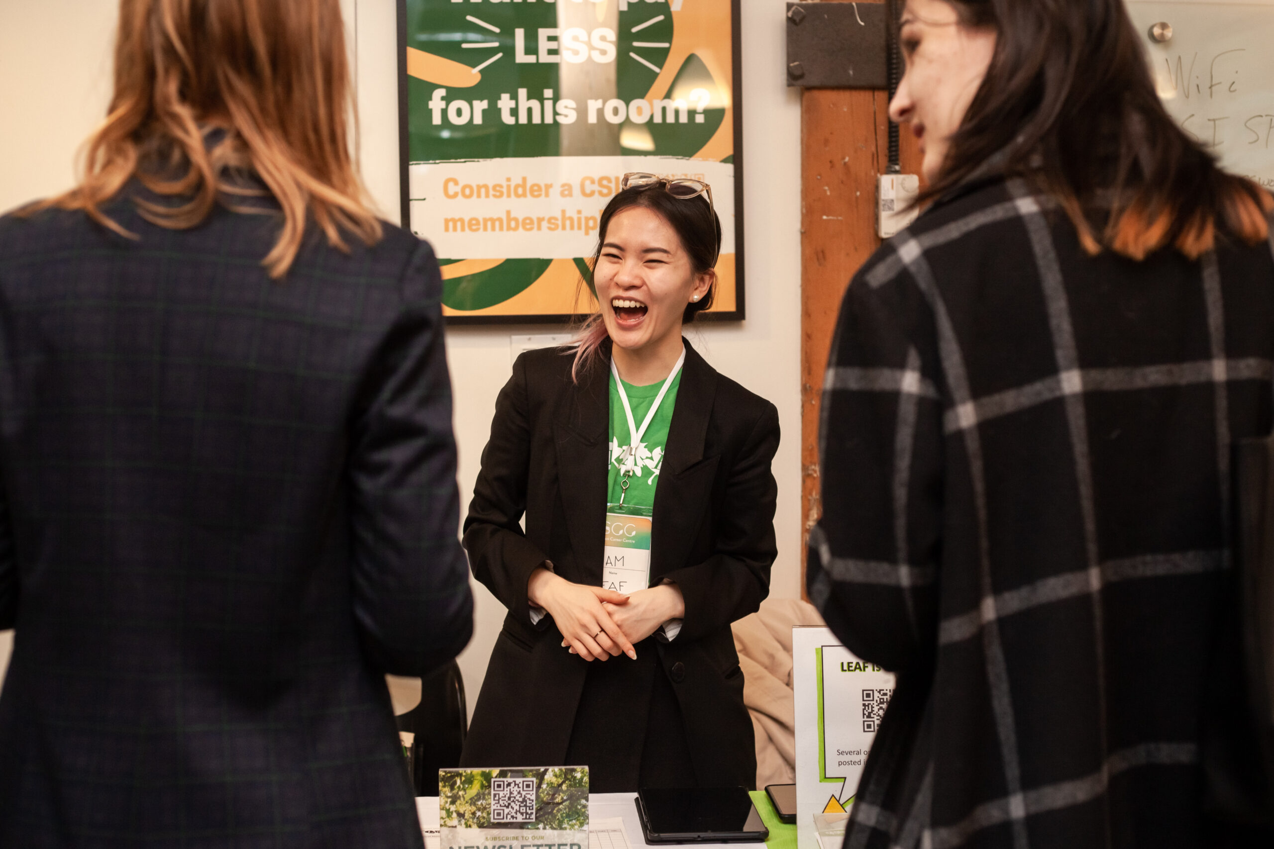 A joyful career fair vendor listens enthusiastically to her engaged attendees
