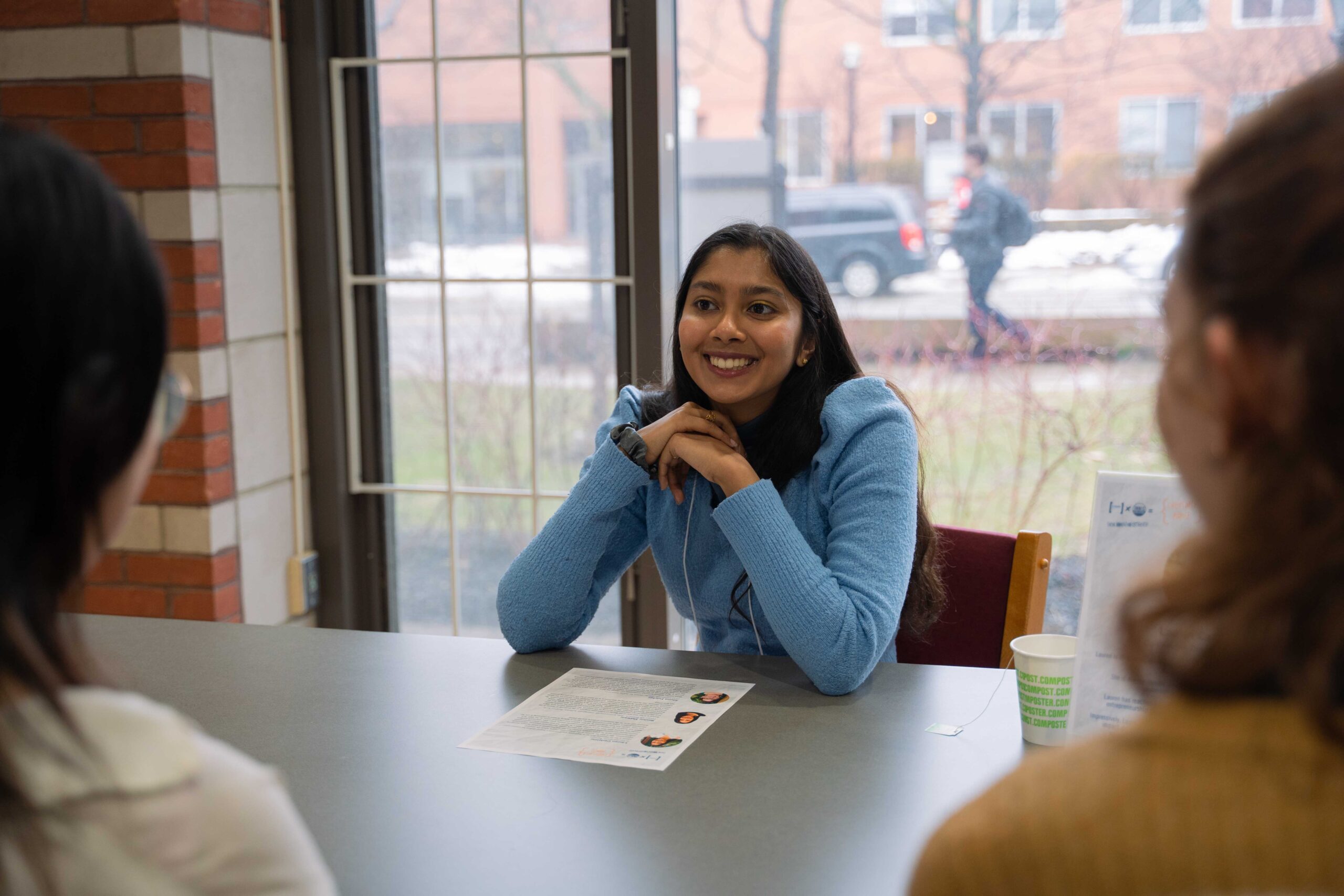 A smiling woman is the focus, with the backs of two women visible as they listen to her