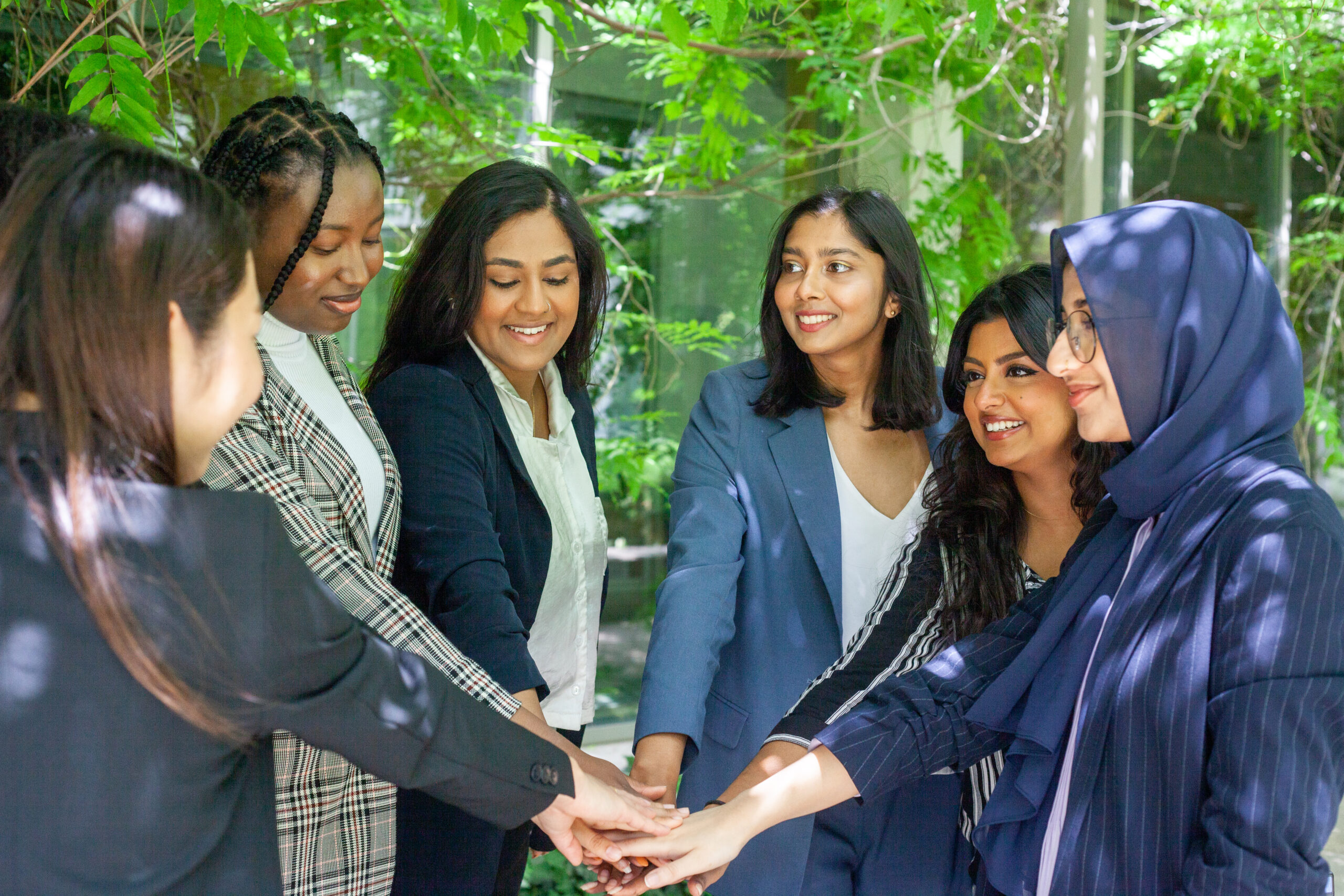 IMG_3413 (2) Team of diverse professional women stacking hands in unity outdoors.